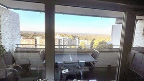 A balcony with a glass partition, a table, chairs, and a view of the cityscape. - Fully furnished apartment with panoramic views of Cologne (Bergisch Gladbach)