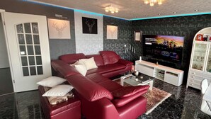 A modern living room with a red sectional sofa, a glass coffee table, and a flat-screen TV. - Fully furnished apartment with panoramic views of Cologne (Bergisch Gladbach)