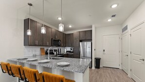 A modern kitchen with granite countertops, dark wooden cabinets, stainless steel appliances, and a central island with bar stools. - Beachy Paradise 1BR/1BA Near Atlantic Beach (Jacksonville)