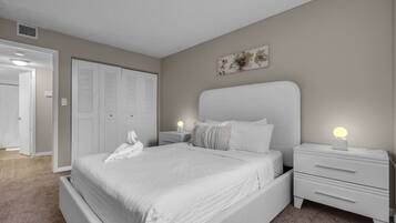 Un dormitorio con una cama grande, dos mesitas de noche con lámparas, un armario y una puerta que da a otra habitación.
