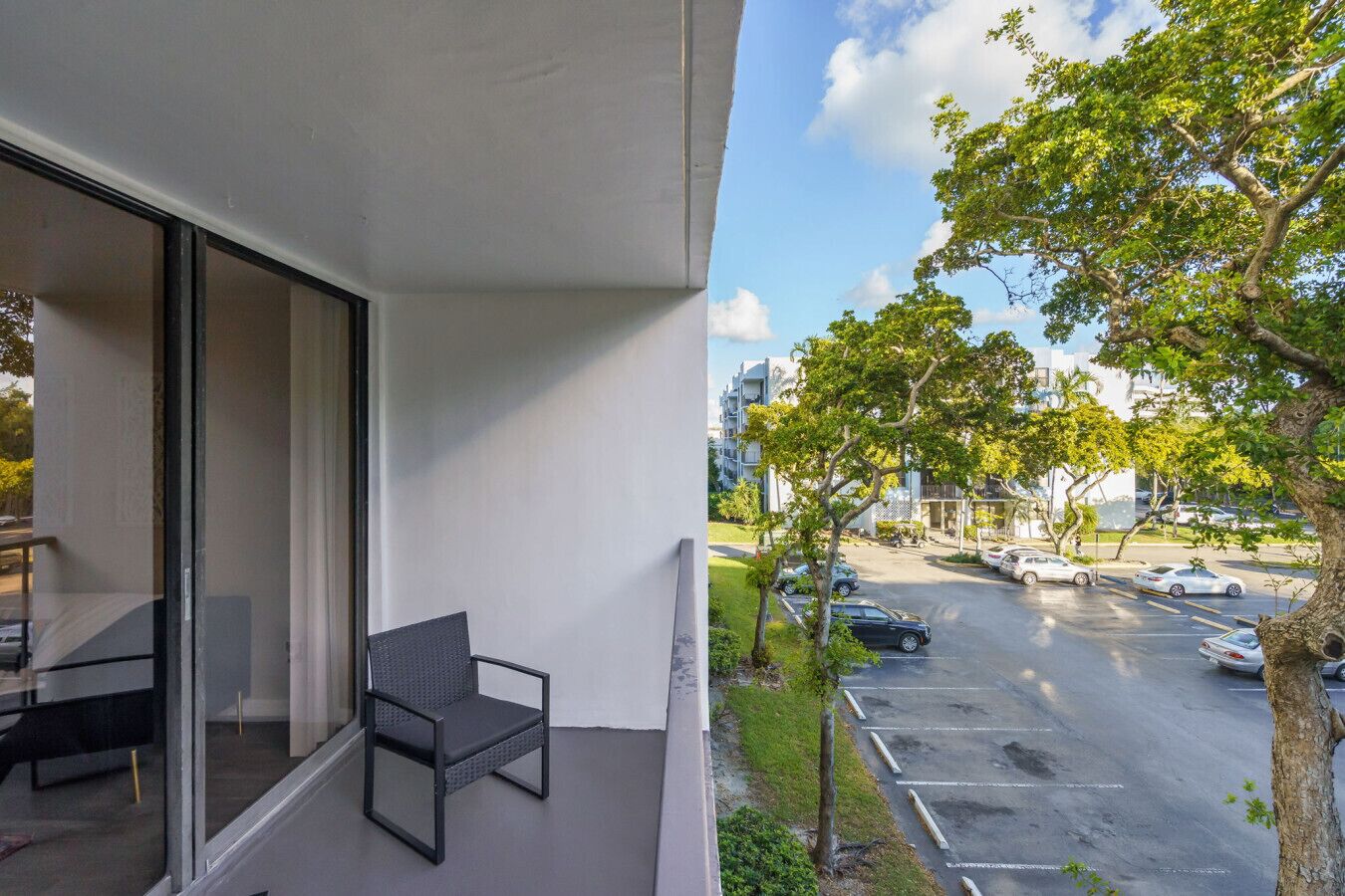 Un balcón con una silla, una mesa y vistas a un estacionamiento y edificios.
