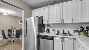 Una cucina moderna con mobili bianchi, elettrodomestici in acciaio inossidabile e un'area pranzo con tavolo e sedie in vetro.
