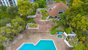 Vista aerea di una piscina circondata dal verde, con un piccolo edificio e un’area di parcheggio sullo sfondo.