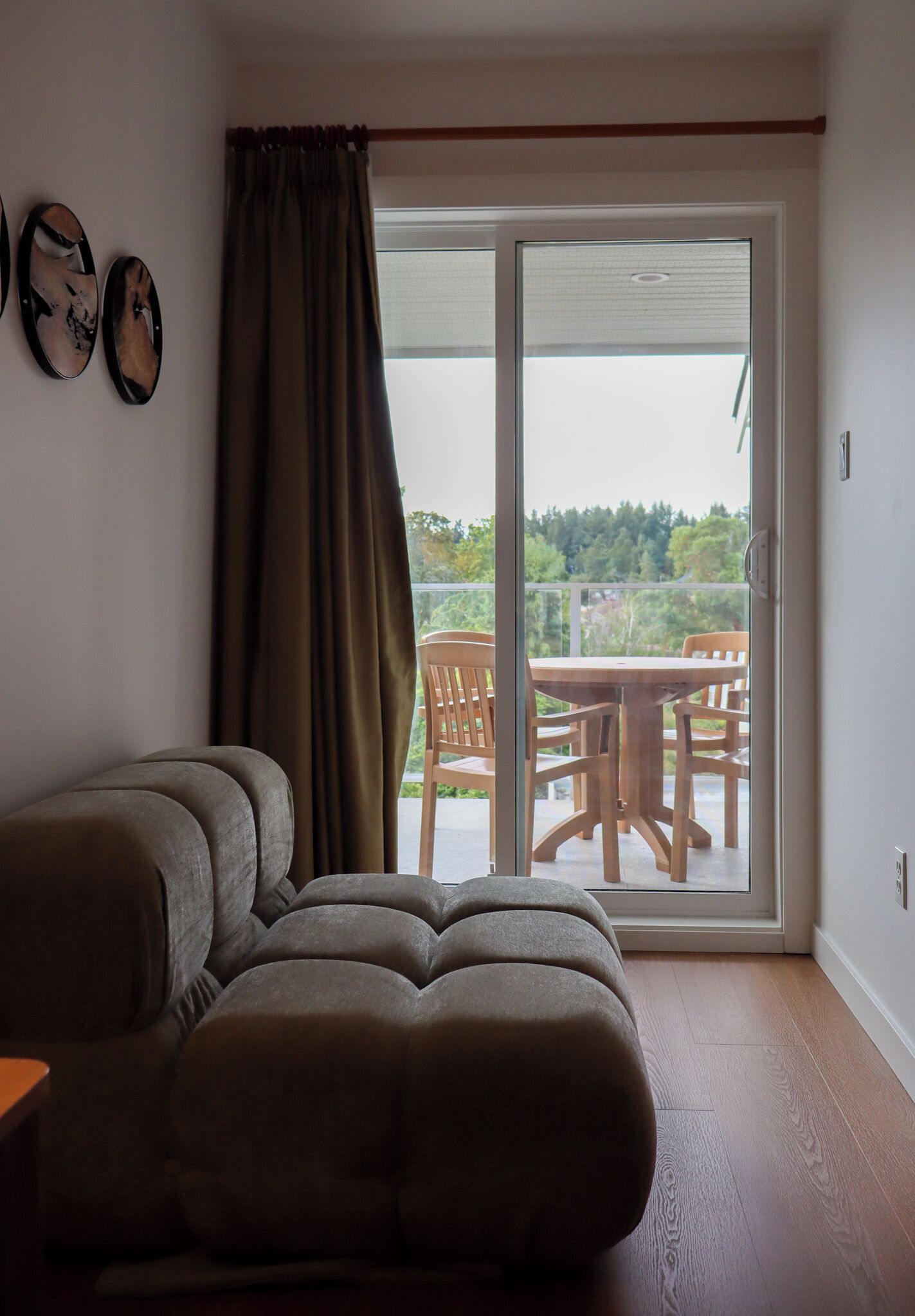 Une pièce comprenant un canapé, un rideau et une porte-fenêtre coulissante donnant sur un espace extérieur avec une table et des chaises.