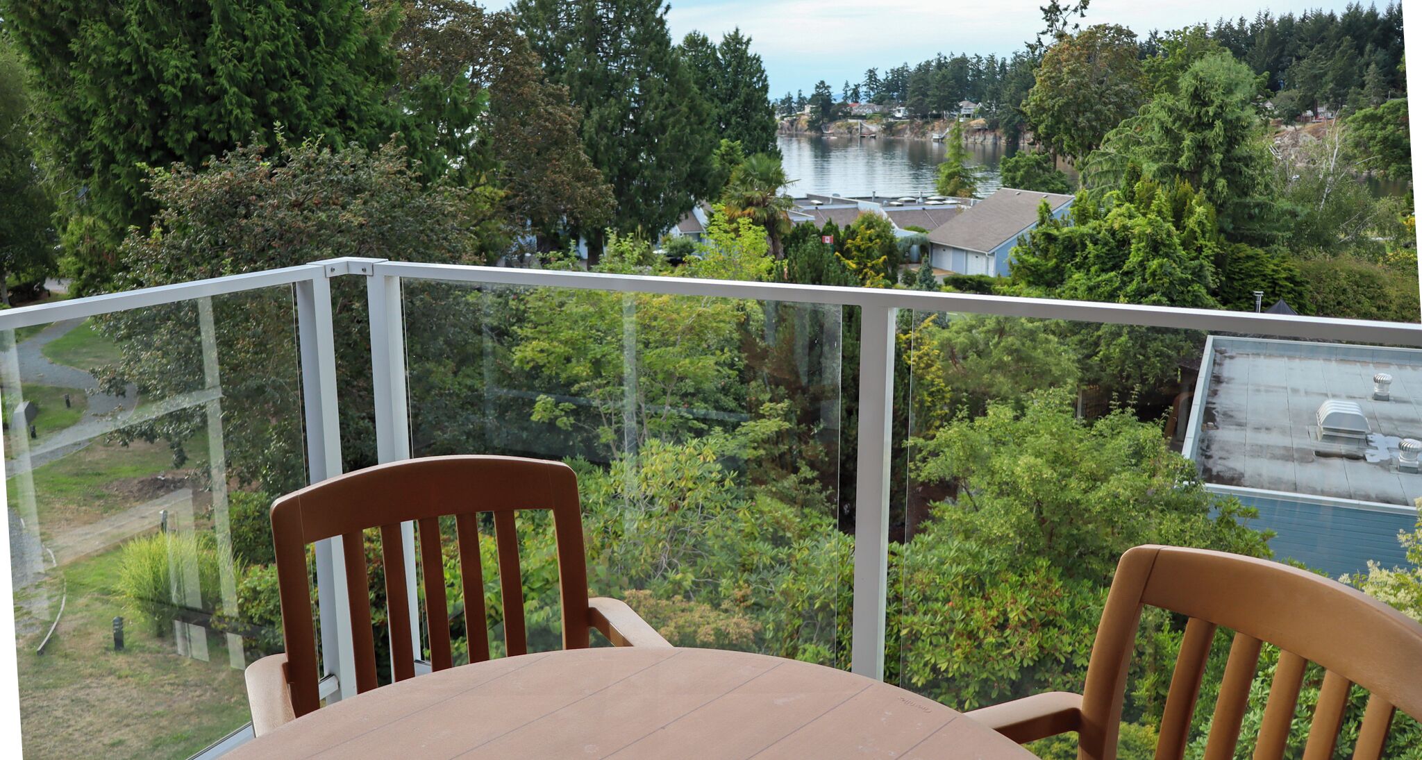 A balcony with a table and chairs, overlooking a lake and forested area.