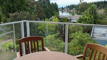 A balcony with a table and chairs, overlooking a lake and forested area.
