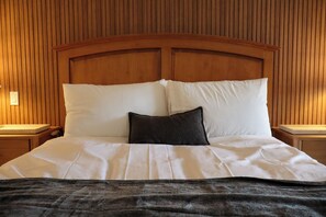 Ein ordentlich bezogenes Bett mit weißen Leinen und einer dunklen Tagesdecke, vor einem holzverkleideten Kopfteil.