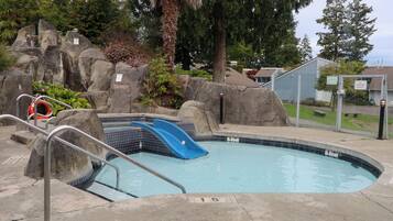 Piscina com escorrega, cercada por pedras e árvores.