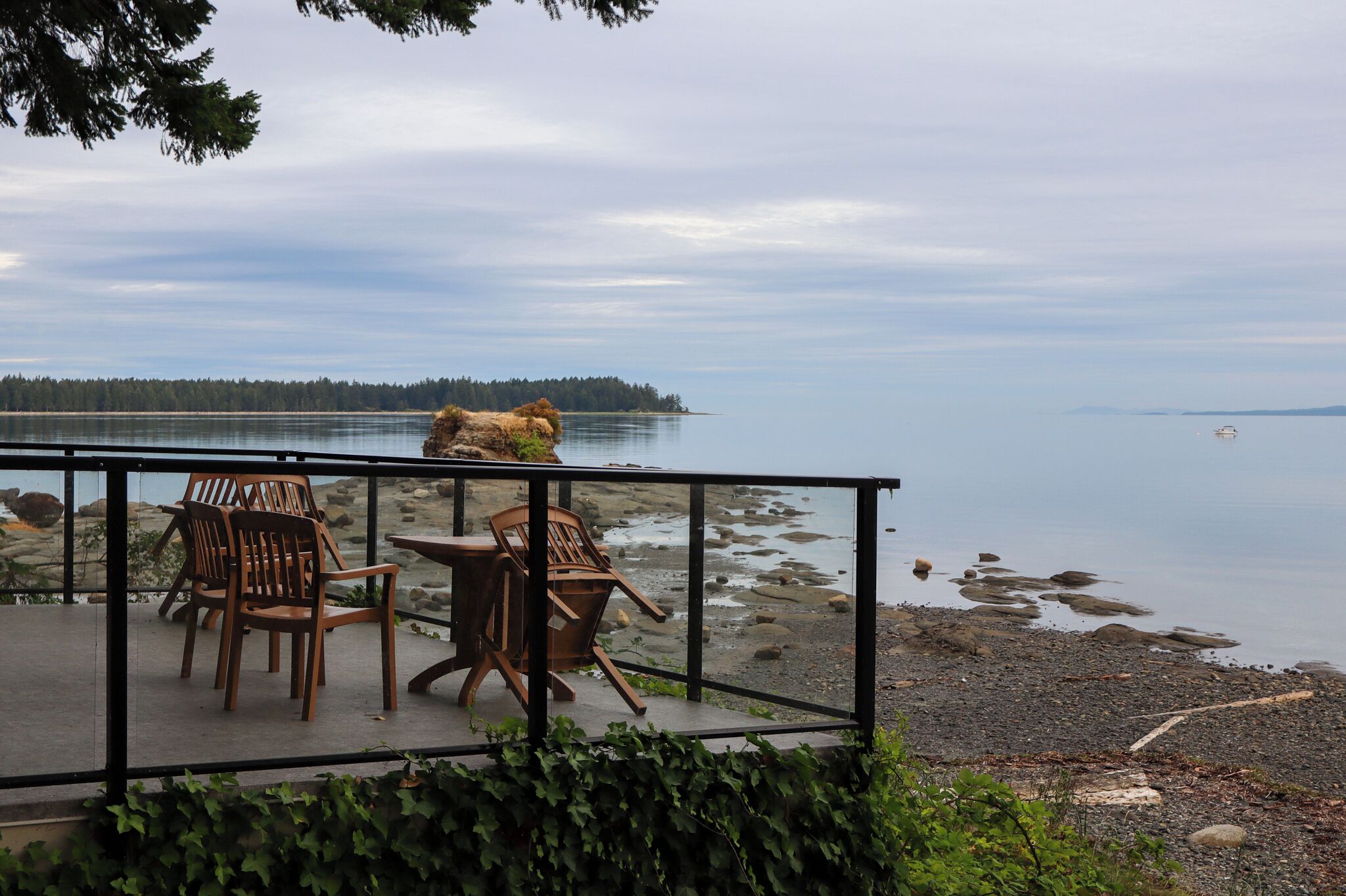 An outdoor seating area with chairs and a table, overlooking a calm body of water and a distant shoreline.