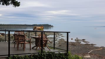 An outdoor seating area with chairs and a table, overlooking a calm body of water and a distant shoreline.