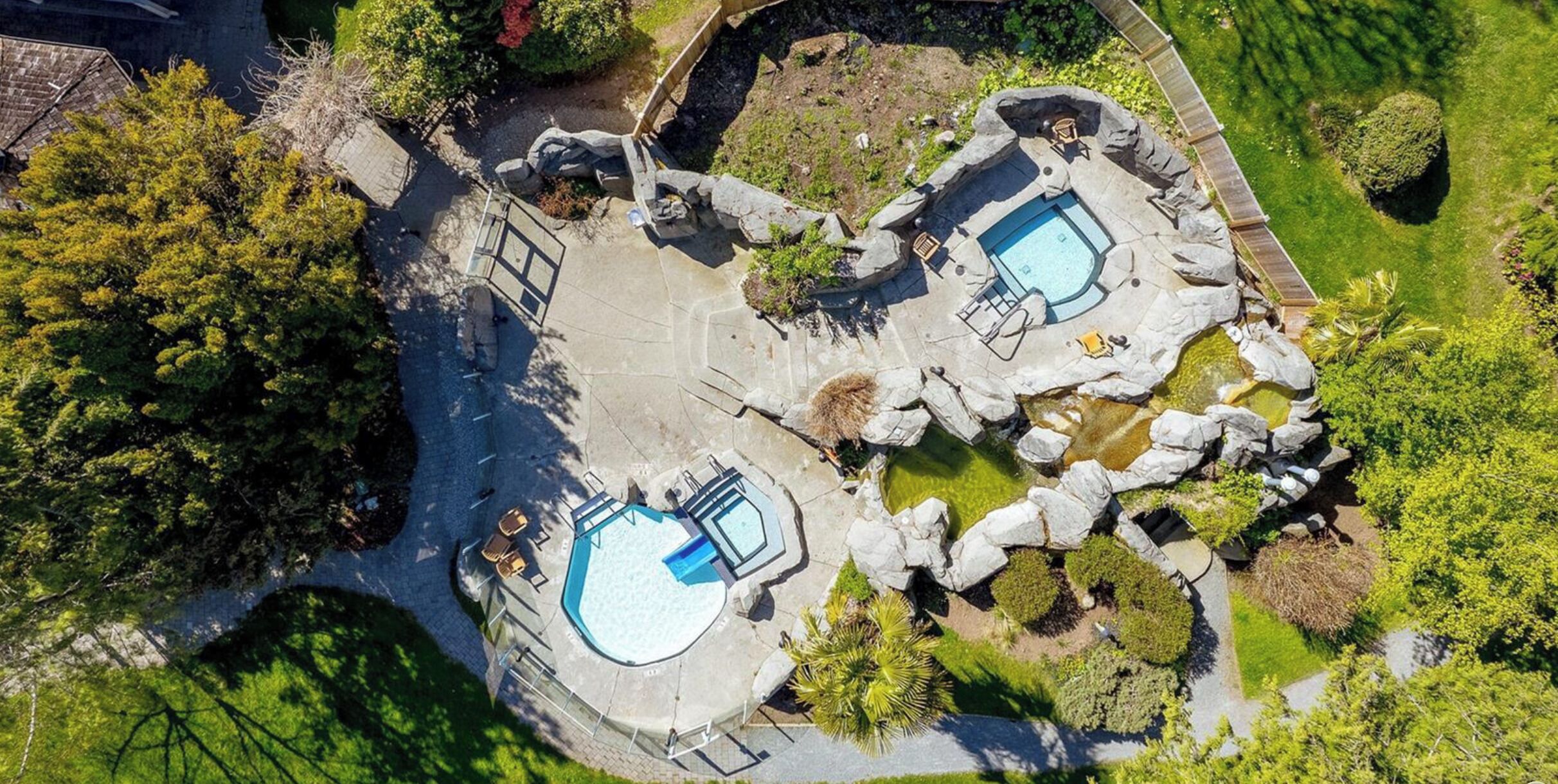 Un espace extérieur doté d’une piscine circulaire, comprenant deux bassins distincts, entouré de rochers et de verdure.
