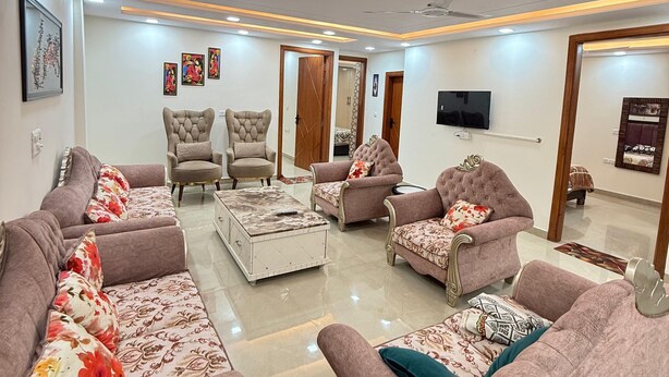 A modern living room with sofas, armchairs, a coffee table, and a television. - Stella Homestay- Near Yashoobhomi (New Delhi)