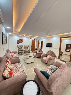 A modern living room with sofas, armchairs, a coffee table, and a television. - Stella Homestay- Near Yashoobhomi  (New Delhi)