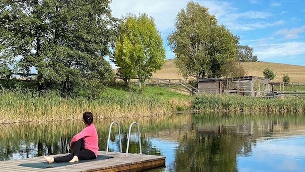 A wooden dock extending into a calm body of water with a person sitting on a mat.