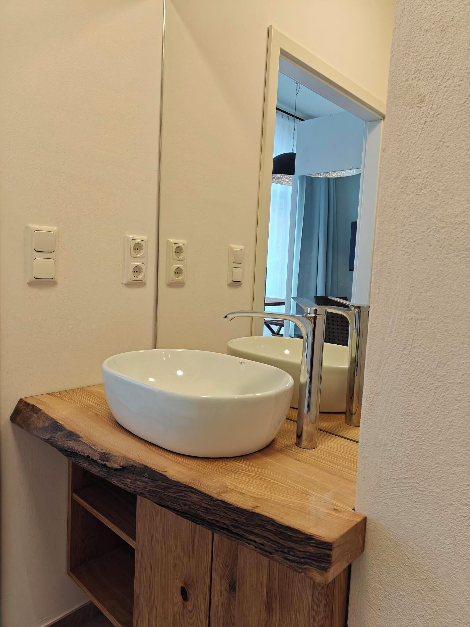 A bathroom with a large white sink, a mirror, and wooden shelves.