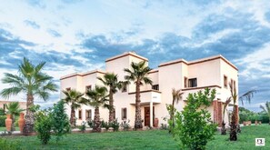 A multi-story building with a flat roof, surrounded by palm trees and greenery.