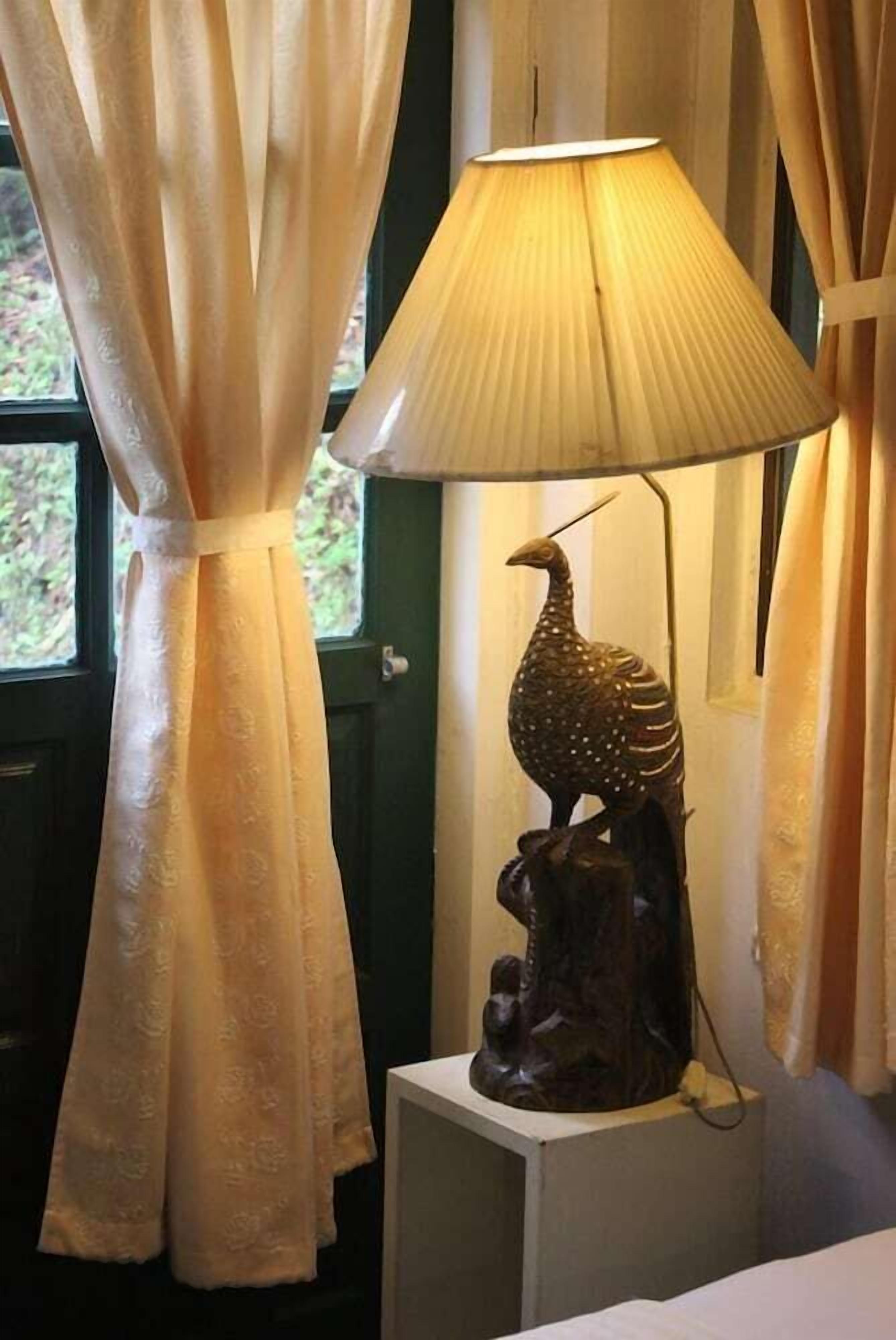 Eine Lampe mit Vogel-Skulptur auf weißem Sockel, ein Fenster mit Vorhängen und eine grüne Tür.