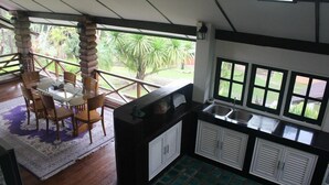 A room with a dining table and chairs, a kitchen area with cabinets and a sink, and large windows offering a view of greenery outside. - The Stove House Hang Dong Chiang Mai (Hang Dong)