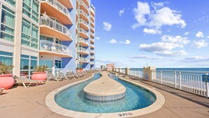 A pool area with lounge chairs and a pool deck, surrounded by a building with balconies and a view of the ocean. - Prince Resort at Cherry Grove Pier with lazy river (North Myrtle Beach)