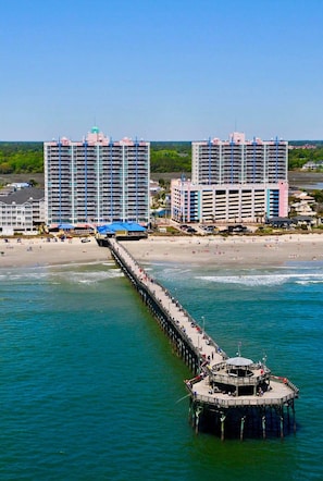A pier extending into the water with buildings in the background. - Prince Resort at Cherry Grove Pier with lazy river (North Myrtle Beach)