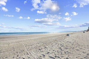 Ampia spiaggia sabbiosa con impronte, cielo sereno e costa in lontananza.