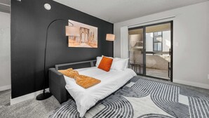 A modern bedroom with a large bed, a black wall, a painting, and a sliding glass door to a balcony. - Pet Frndly Comfortable  2BR Near ASU Pool Grill Prking (Tempe)