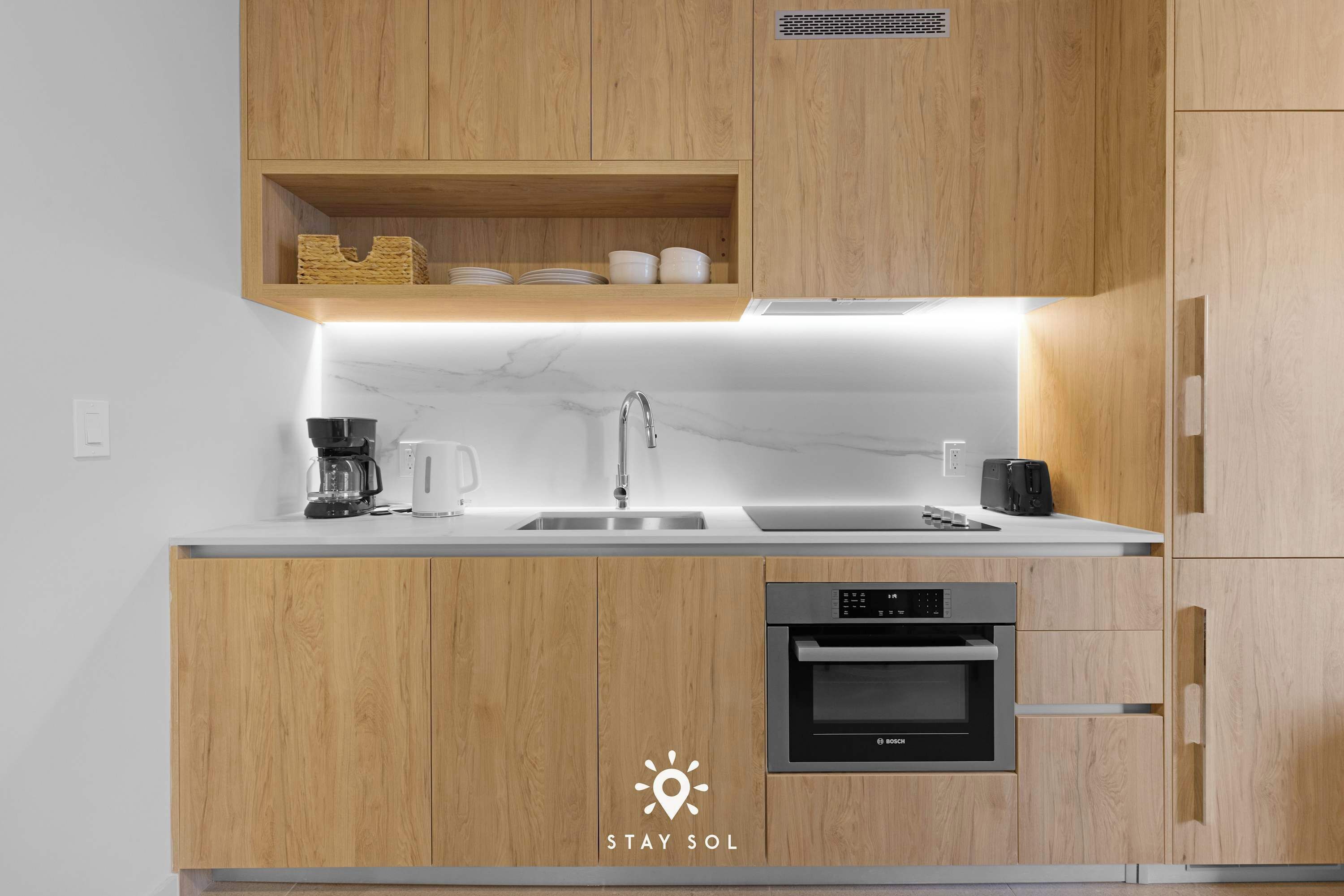A modern kitchen with wooden cabinets, a built-in oven, and a coffee maker.