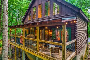 A log cabin with a deck, large windows, and string lights. - Treetop Hot Tub Retreat • King Suite • Foosball+Arcade • Close to everything (Sevierville)