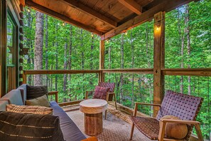 A wooden deck with a sofa, chairs, and a round table, overlooking a forest. - Treetop Hot Tub Retreat • King Suite • Foosball+Arcade • Close to everything (Sevierville)