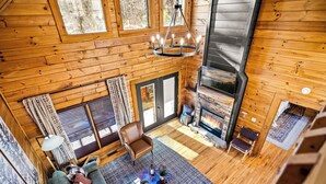 Ein gemütliches Blockhauss-Interieur mit Holzausstattung, Kamin, einer Couch und einem Esstisch.