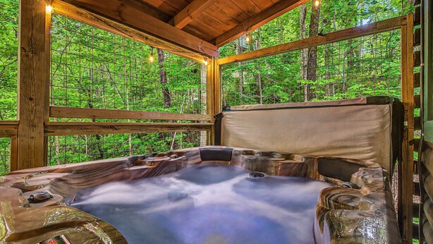 Ein Whirlpool mit Bedienfeld, umgeben von Holzbalken und großen Fenstern mit Blick auf einen Wald.