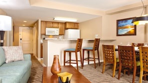 Un espacio habitable compacto con kitchenette, zona de comedor y área de estar con sofá y sillones.