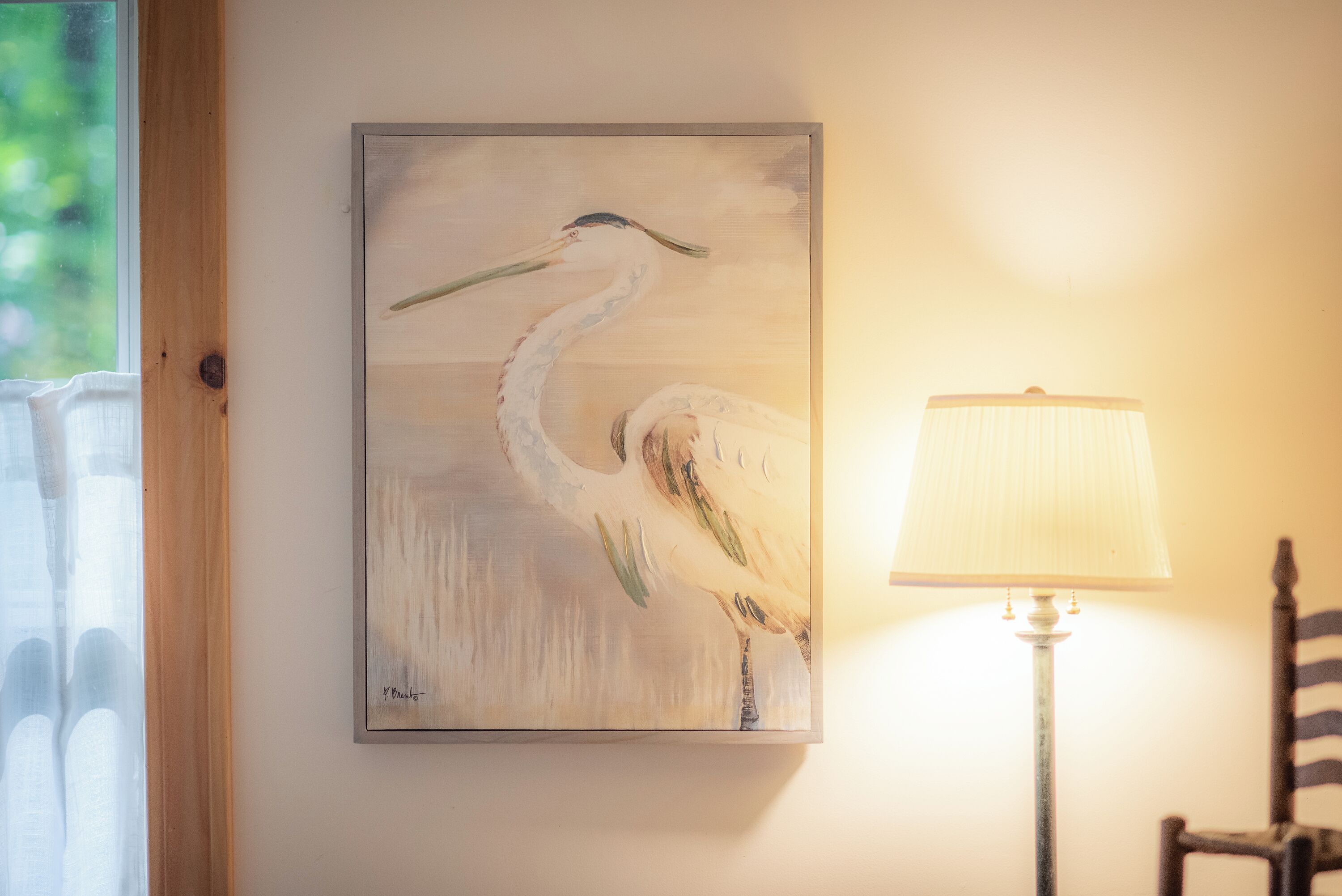 A painting of a heron on a wall, a lamp, and a chair.