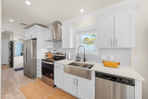 A modern kitchen with white cabinets, stainless steel appliances, and a window with a view of palm trees. - Water Front Sunset 1-Bedroom House fully furnished in perfect Jensen Beach (Jensen Beach)