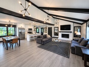 A modern kitchen with a central island, a dining area with a table and chairs, a living room with a sofa and a coffee table, and a fireplace. - Charming 3 Bedroom Ranch in Keystone at the Crossing (Indianapolis)