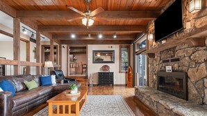 A spacious living room with a stone fireplace, leather sofa, and a ceiling fan.