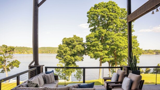 A covered deck with wicker furniture and a view of a lake.
