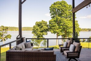 Une terrasse couverte, aménagée avec des meubles en osier, et offrant une vue sur un lac.