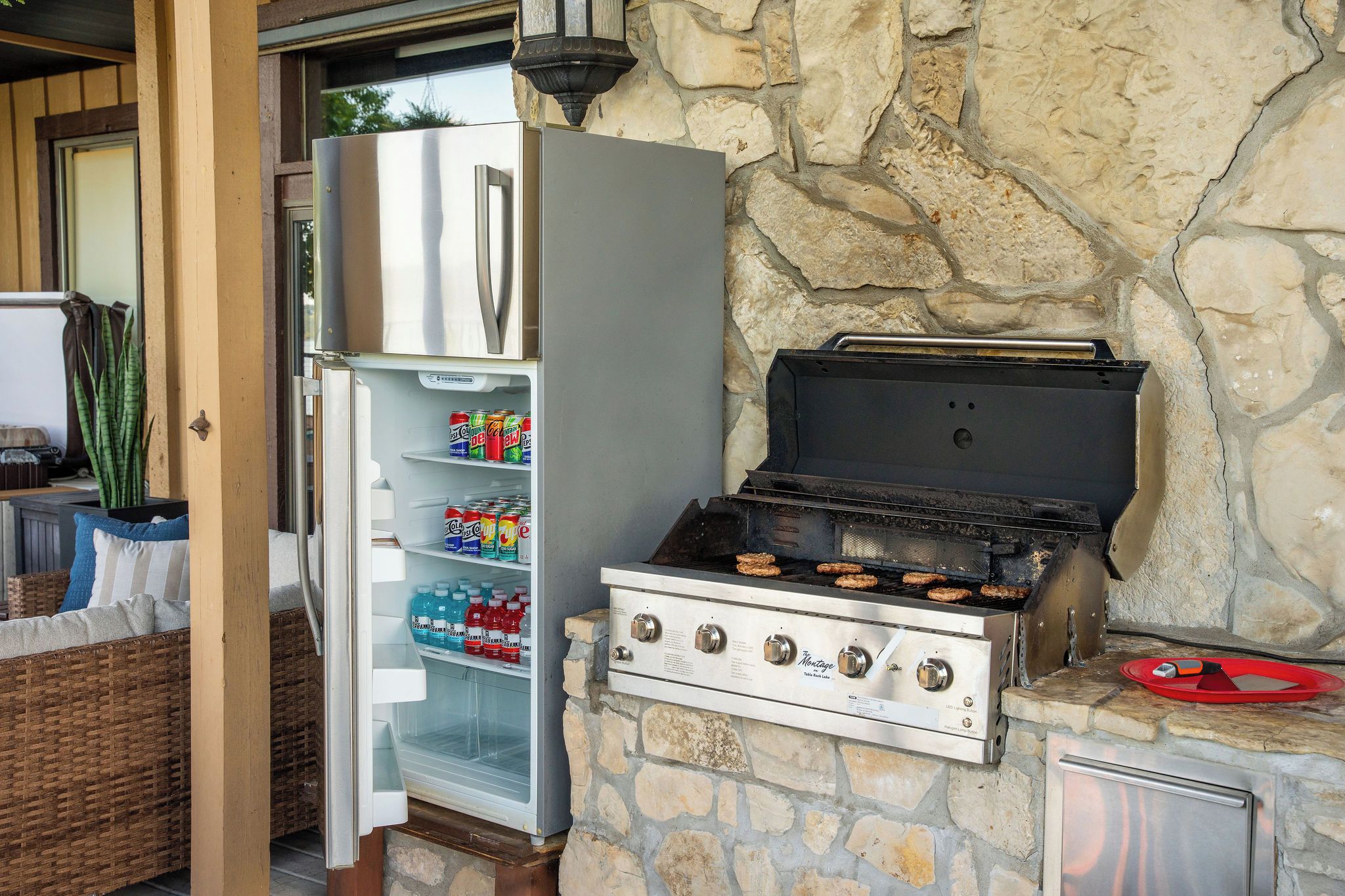 A stone wall with a grill, a refrigerator, and a wicker sofa.
