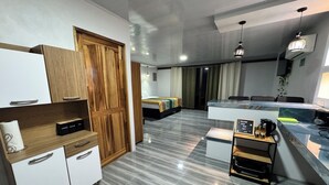 Ein modernes Hotelzimmer mit einem Holzschrank, einem Bett mit grüner und gelber Decke, einer kleinen Küchenzeile und einer Sitzecke mit einer Kaffeemaschine.