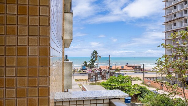Une vue d’une plage, avec un ciel dégagé, un palmier et un bâtiment aux murs recouverts de tuiles.