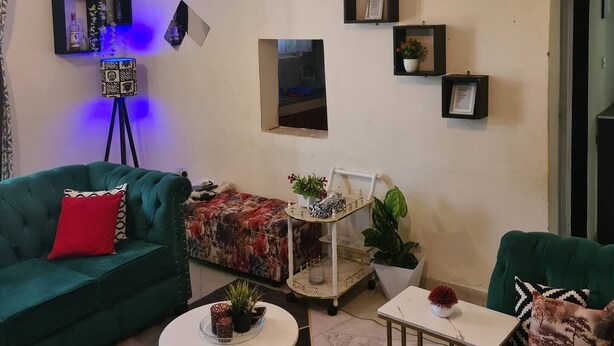 Uma sala de estar com um sofá verde, uma mesa redonda pequena e um ventilador de teto.