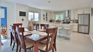 A modern kitchen with white cabinets, a stainless steel refrigerator, and a dining area with wooden chairs and a table. - Cozy Georgian Bay Cottage Firepit, Beach, 4-Seasons (Wahnekewaning Beach)