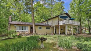 A two-story house with a covered porch and a garden in front. - Cozy Georgian Bay Cottage Firepit, Beach, 4-Seasons (Wahnekewaning Beach)