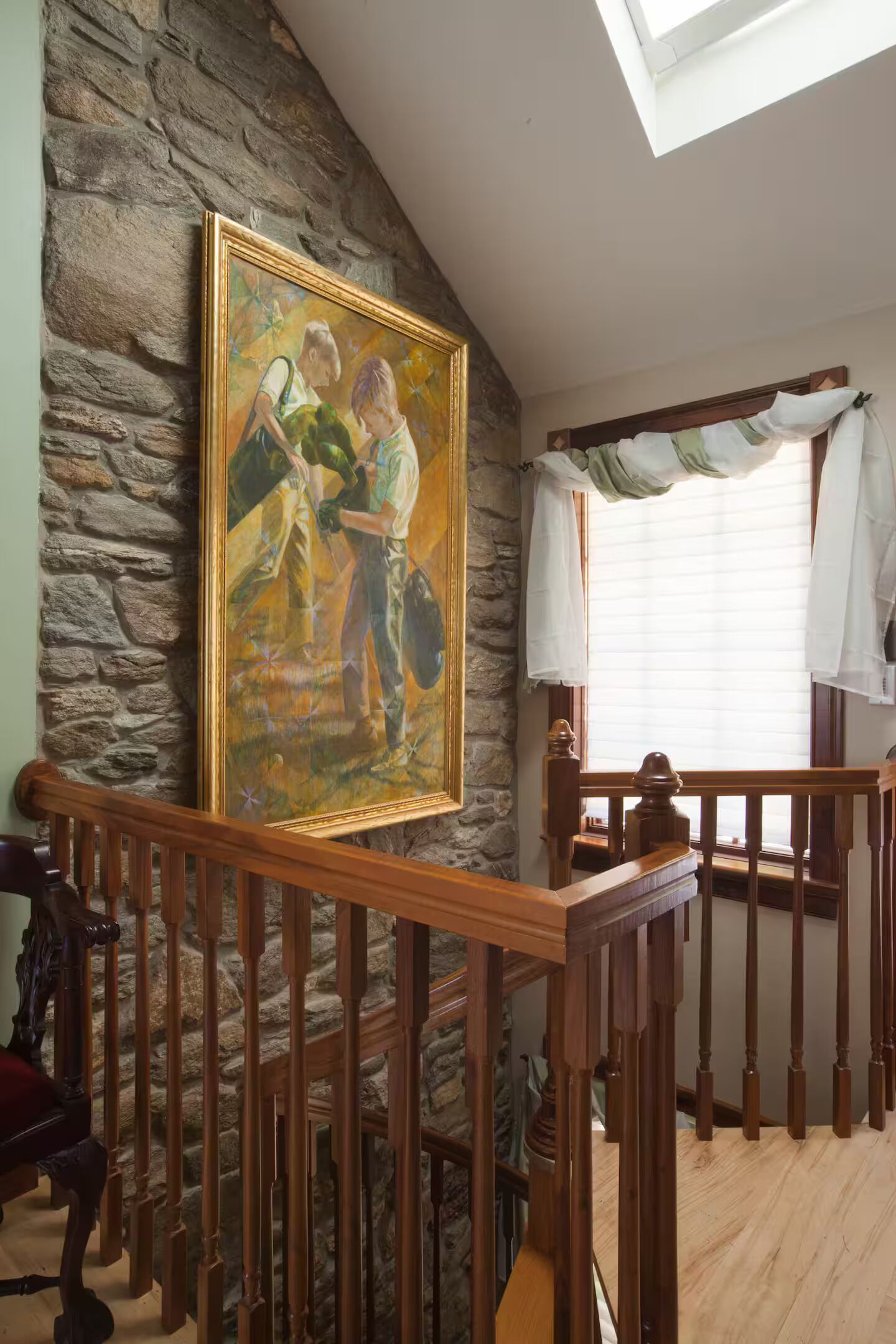 A room with a stone wall, a wooden staircase, and a painting.