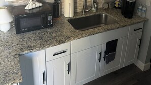 Eine moderne Küche mit weißen Schränken, einer Arbeitsplatte aus Granit, einer Edelstahlspüle und einer Mikrowelle.