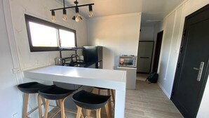 Una cocina moderna con una isla blanca, taburetes de bar, un refrigerador negro, un tostador y una ventana.