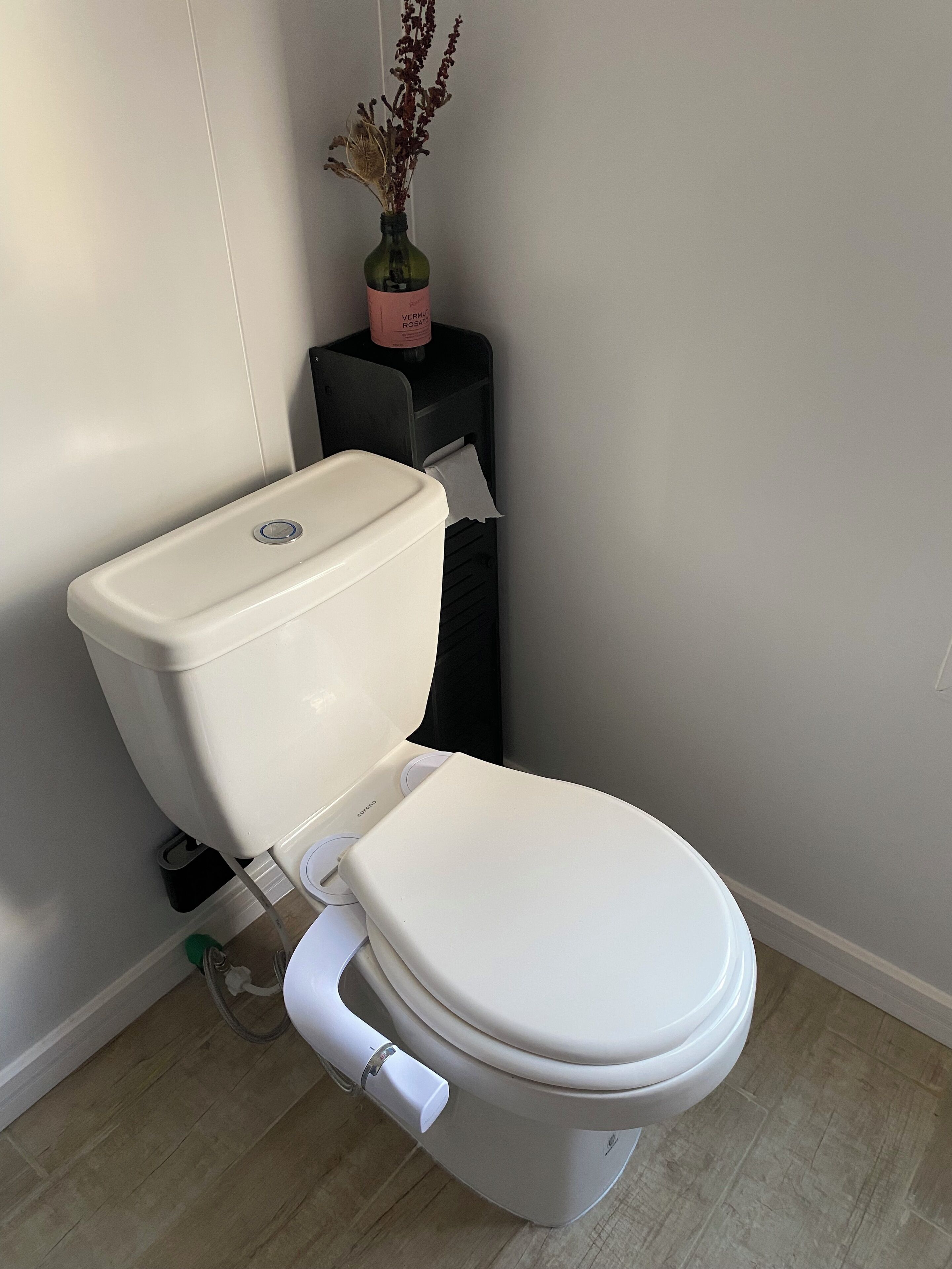 Eine Toilette mit weißem Sitz und Deckel, einem schwarzen Toilettenpapierhalter und einer Flasche Toilettenreiniger darauf.