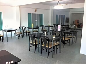 A spacious dining area with multiple tables and chairs, a ceiling fan, and a view of the dining area through a glass partition. - S K Airport (Chiang Mai)