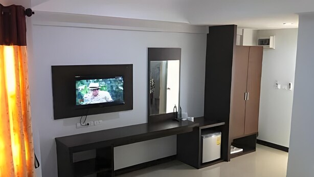 A modern hotel room with a flat-screen TV mounted on the wall, a built-in vanity with a mirror, a dark wooden wardrobe, and a small bedside table. - S K Airport (Chiang Mai)